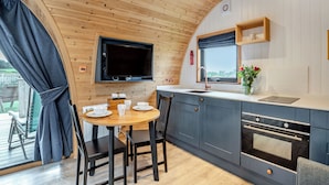 A compact kitchen with a dining area, wooden ceiling, and a TV mounted above the counter.
