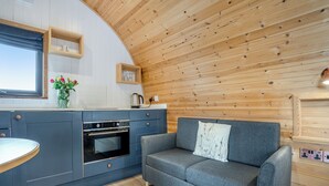 A modern kitchen with a built-in oven, a grey sofa with a decorative pillow, and wooden paneling on the ceiling.