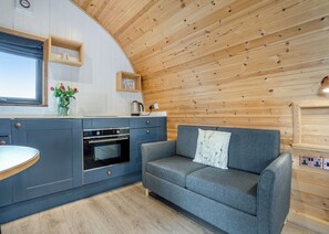 Une cuisine moderne dotée d’un four encastré, d’un canapé gris agrémenté d’un coussin décoratif et de lambris en bois au plafond.
