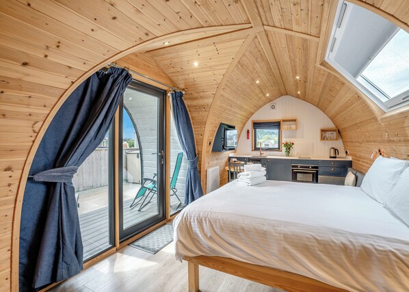 Un interior acogedor de madera con una cama, una kitchenette pequeña y un ventanal corredero que da a un espacio exterior.