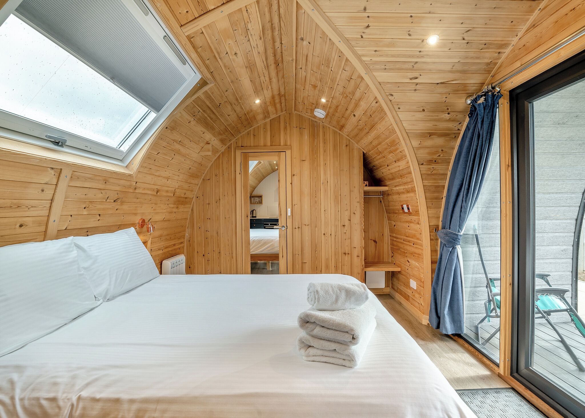 Une pièce chaleureuse, avec des murs en bois, un lit, une fenêtre et une vue sur l’extérieur.