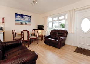 A living room with a fireplace, a dining area with chairs, a sofa, a television, and a window with curtains. - Bungalow with one double and one single. (Trearddur Bay, Holyhead)
