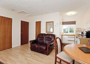 A room with a leather sofa, wooden dining table, and a kitchen area with appliances.