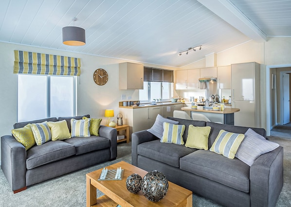A modern living room with two grey sofas, a wooden coffee table, and a kitchen in the background.