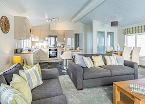 A modern living room with a grey sofa, a wooden coffee table, and a kitchen in the background.