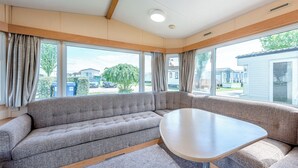 Une pièce comprenant un grand canapé d’angle, une table ronde et de grandes fenêtres donnant sur un quartier résidentiel.