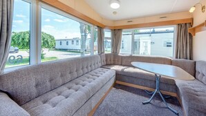 A cozy RV interior with a sectional sofa, a small table, and large windows offering a view of the outside.