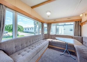 Interior acogedor de una autocaravana con un sofá modular, una mesita y grandes ventanales que ofrecen vistas al exterior.