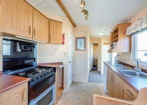 Una cocina compacta con armarios de madera, estufa, microondas y pileta.