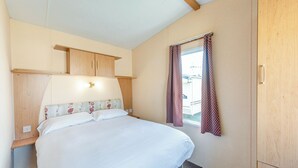 Une chambre à coucher avec un lit, une tête de lit en bois, une fenêtre avec des rideaux, un luminaire au plafond et une armoire en bois.