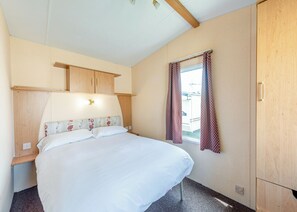 Ein Schlafzimmer mit Bett, Holz-Kopfteil, einem Fenster mit Vorhängen, einer Deckenleuchte und einem Holzschrank.