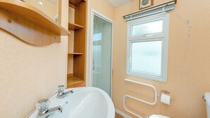 Une salle de bain avec un lavabo blanc, des toilettes, une fenêtre et une étagère en bois.