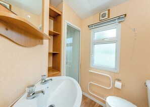 Ein Badezimmer mit weißem Waschbecken, Toilette, Fenster und Holzregal.