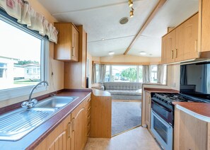 A compact kitchen with a sink, stove, and wooden cabinets. - Caravan with one double and one twin. (Bognor Regis)