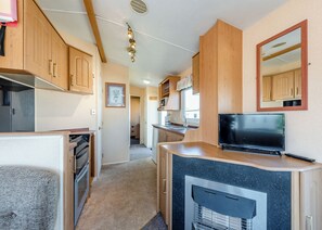Eine kleine Küche mit Holzschränken, einem eingebauten Backofen, einer Mikrowelle, einem Spülbecken und einem Fernseher.