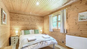 Une pièce aux murs lambrissés, comprenant un lit, des tables de chevet, un radiateur et une fenêtre avec des rideaux.