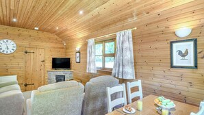L’intérieur d’un chalet en bois, avec un canapé, des fauteuils, une table à manger où est servi le petit-déjeuner, un téléviseur et une cheminée.