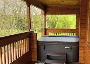 A wooden cabin with a hot tub, a small step, and a window overlooking greenery. - Stunning lodge built on the edge of the lake. (Anglesey)