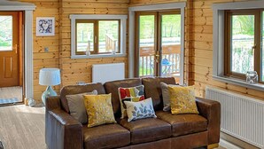Interior de una cabaña de madera con un sofá de cuero, una lámpara y vistas al exterior.