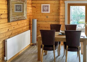 A wooden interior with a dining table, four chairs, a radiator, and framed pictures on the wall. - Stunning lodge built on the edge of the lake. (Anglesey)