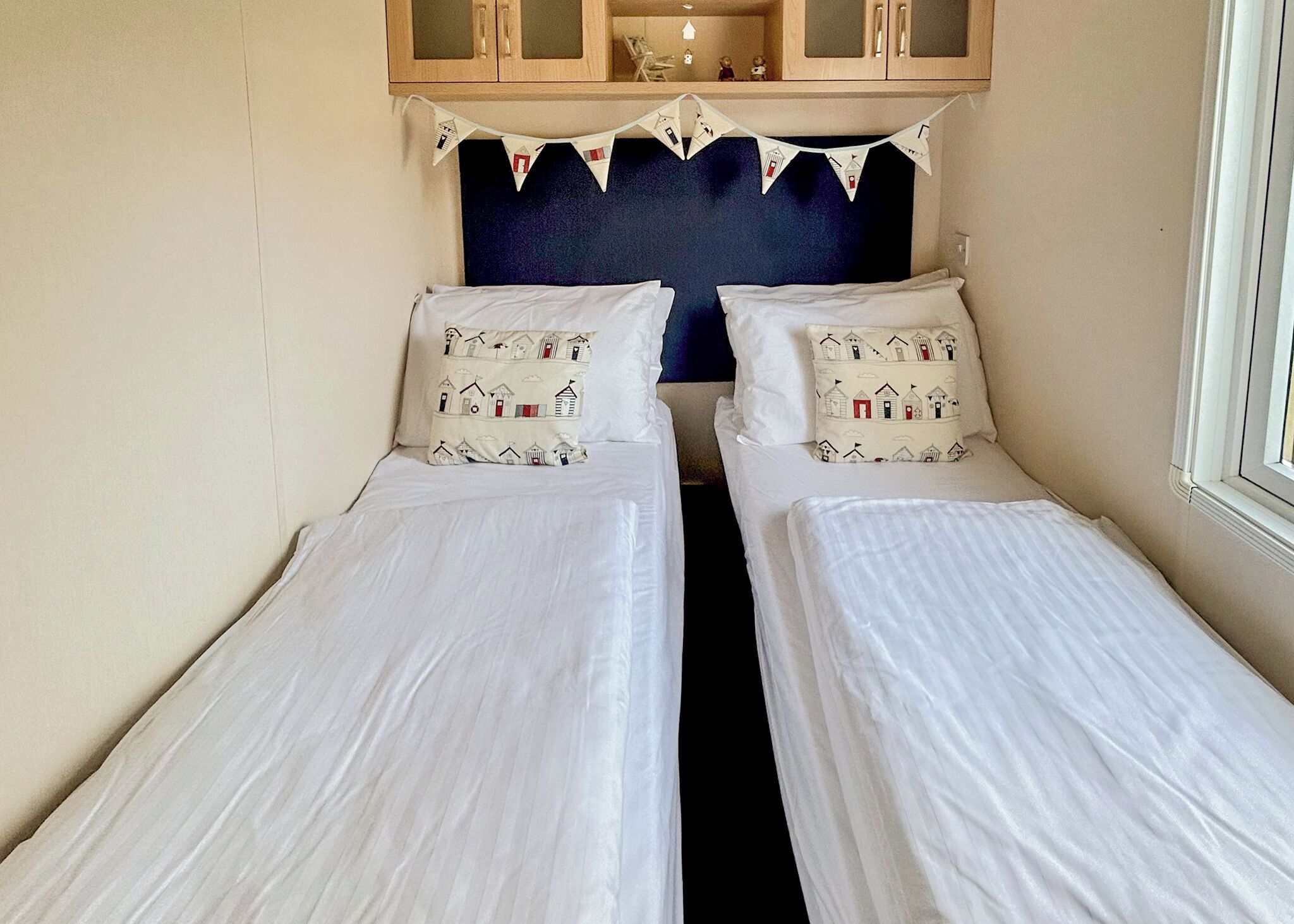 A room with two single beds, a dark headboard, and a small cabinet above.