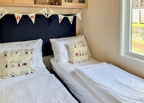 Un dormitorio con dos camas, cada una con almohadas a juego, un cabecero oscuro y una ventana con vistas a un jardín.