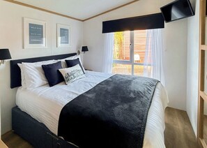 A bedroom with a bed, a window with blinds, two wall-mounted lamps, and two framed signs on the wall. - Country Holiday Home Four (Tintagel)