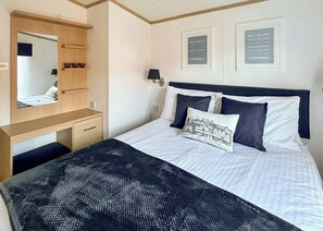 Un dormitorio con cama, mesita de noche, espejo y dos carteles enmarcados en la pared.