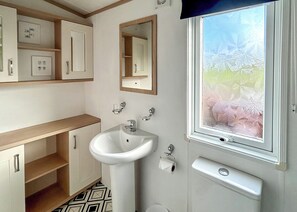 A bathroom with a sink, mirror, toilet, and a window with a view of trees. - Country Holiday Home Four (Tintagel)