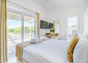 A hotel room with a bed, a desk, a TV, and a balcony with a view.