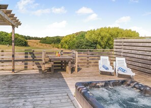 An outdoor deck with a hot tub, wooden furniture, and lounge chairs.
