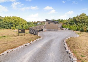 Ein Kiesweg führt zu einer Lodge mit einer Holzterrasse und einem kleinen Gebäude.