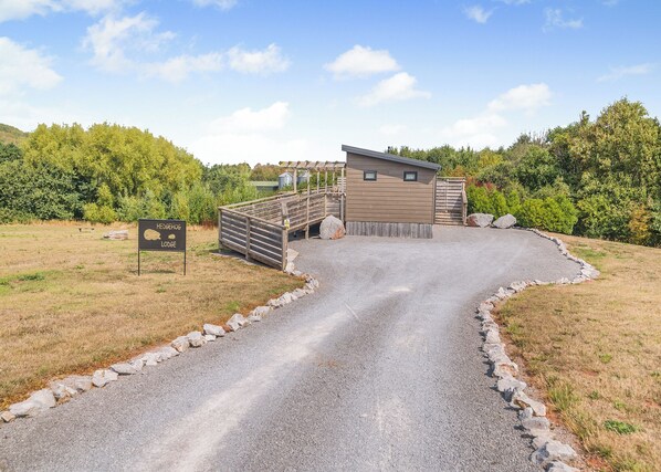 A gravel path leading to a lodge with a wooden deck and a small building. - 1 bedroom accommodation in Cannington (Cannington)