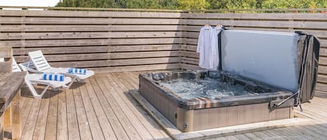 A wooden deck with lounge chairs and a hot tub.