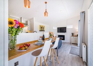 A modern kitchen with a dining area, white cabinetry, a fireplace, and a television.