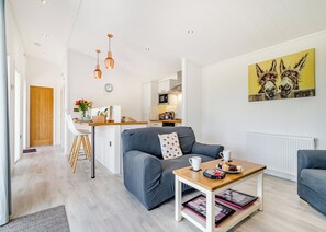 Un salon moderne avec un canapé gris, une table basse en bois et un coin cuisine à l’arrière-plan.