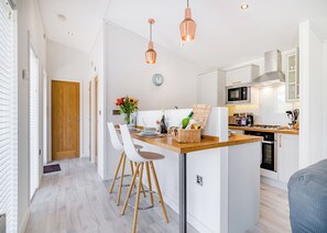 A modern kitchen with a central island, wooden chairs, a dining table, and pendant lighting. - 1 bedroom accommodation in Cannington (Cannington)