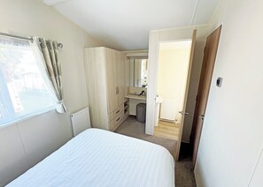 Une chambre à coucher avec un lit, une armoire, un miroir, un radiateur et une salle de bain visible à travers une porte ouverte.