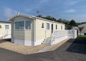Une maison mobile de plain-pied, dotée d’un porche à l’avant, d’un petit escalier et d’une antenne parabolique.