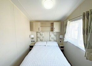 A single bed with a headboard, two bedside tables with lamps, a ceiling light, and a window with curtains.