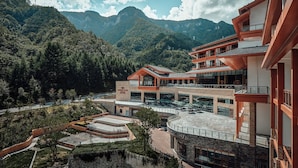 A modern building with multiple floors, outdoor seating areas, and a view of a mountainous landscape. - Crowne Plaza Shennongjia by IHG (Shennongjia)