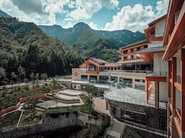 Un edificio moderno con varios pisos, zonas de estar al aire libre y vistas a un paisaje montañoso.
