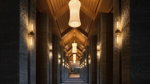 Un pasillo con vigas de madera y paredes de piedra, con iluminación colgante y apliques.