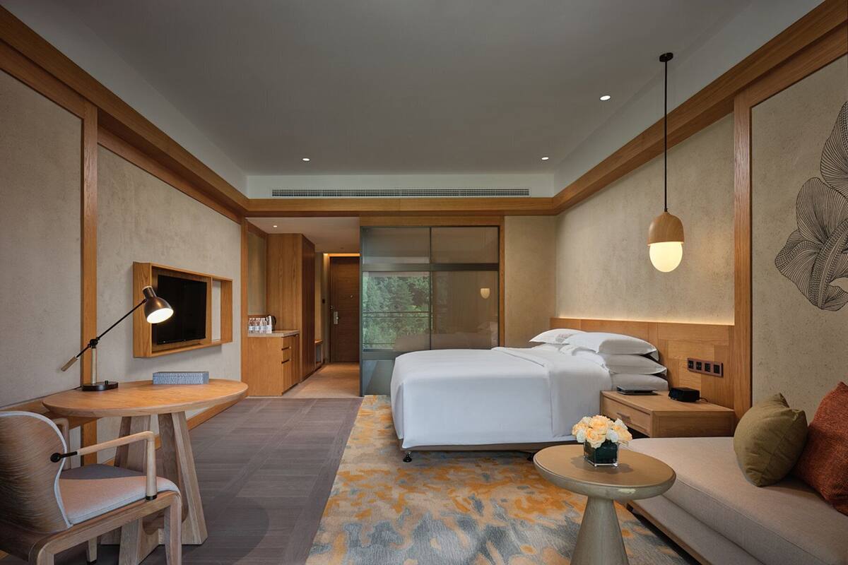 Una habitación de hotel moderna con cama, escritorio, sillón, sofá y una pequeña mesa con flores.