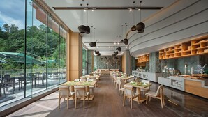 Un restaurante espacioso con techos altos, amplias ventanas y una larga zona de comedor con mesas y sillas de madera.