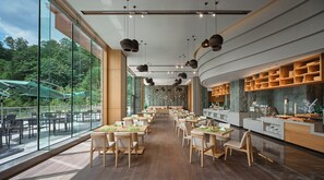 Un restaurant spacieux avec de hauts plafonds, de grandes fenêtres et une vaste salle à manger dotée de tables et de chaises en bois.