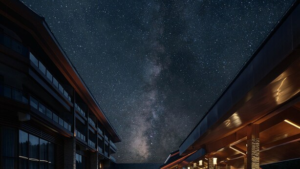 Un hotel con un área exterior techada, ventanas amplias y vista al cielo nocturno.