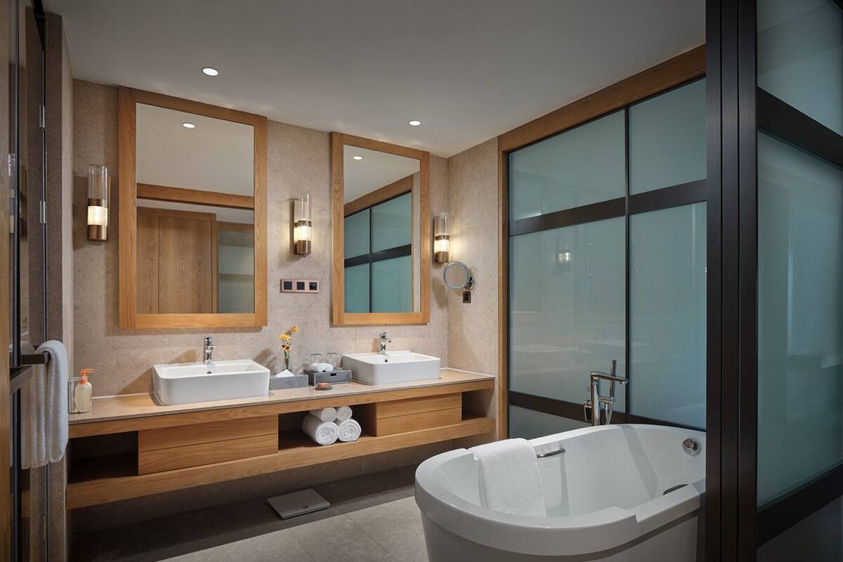 Un baño moderno con dos lavabos, una bañera grande y un box de ducha con mampara de cristal.
