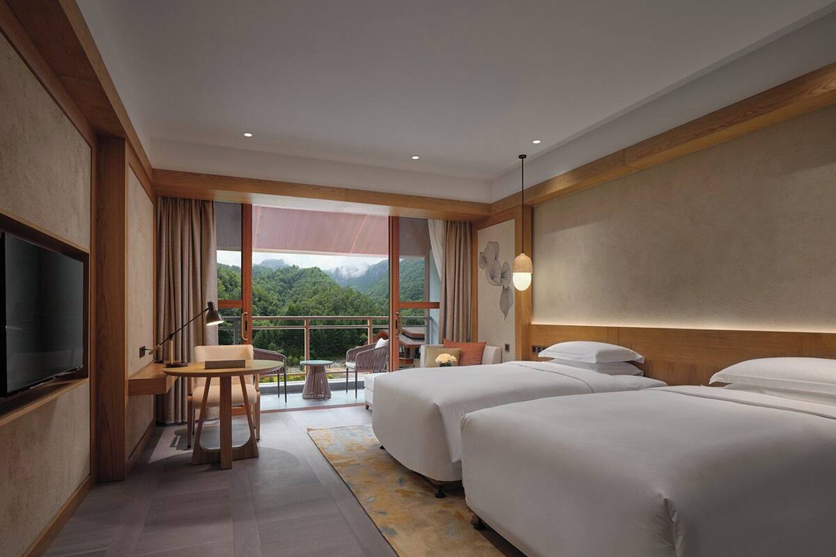 Una habitación de hotel con balcón, dos camas, un escritorio y una televisión.