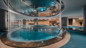 Una piscina interior moderna de diseño circular, con varios niveles y cerramiento de vidrio.